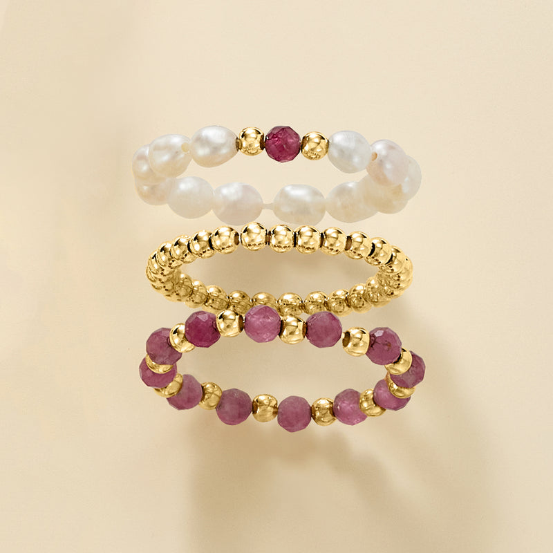 Three stretch rings layered: white pearl ring, pink stone ring, yellow gold bead ring