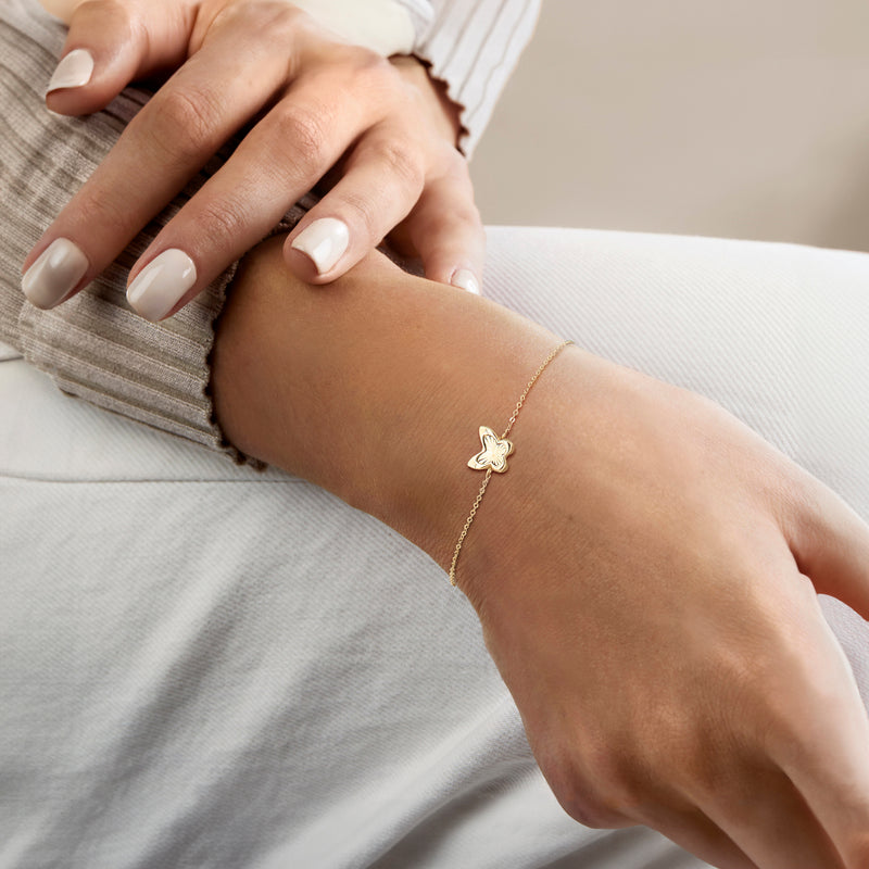 Yellow gold butterfly charm bracelet worn on wrist with delicate chain