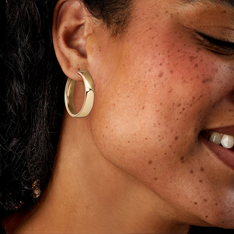 Gold-plated hoop earrings worn on ear, oval hoop with hinged closure