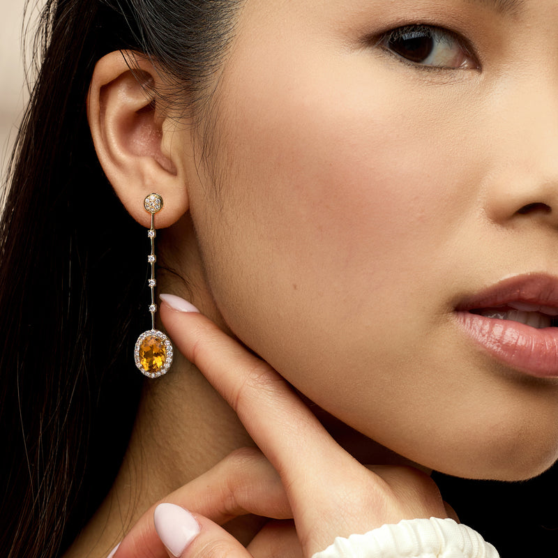 Yellow gold drop earrings with oval citrine center and diamond line accents on ear