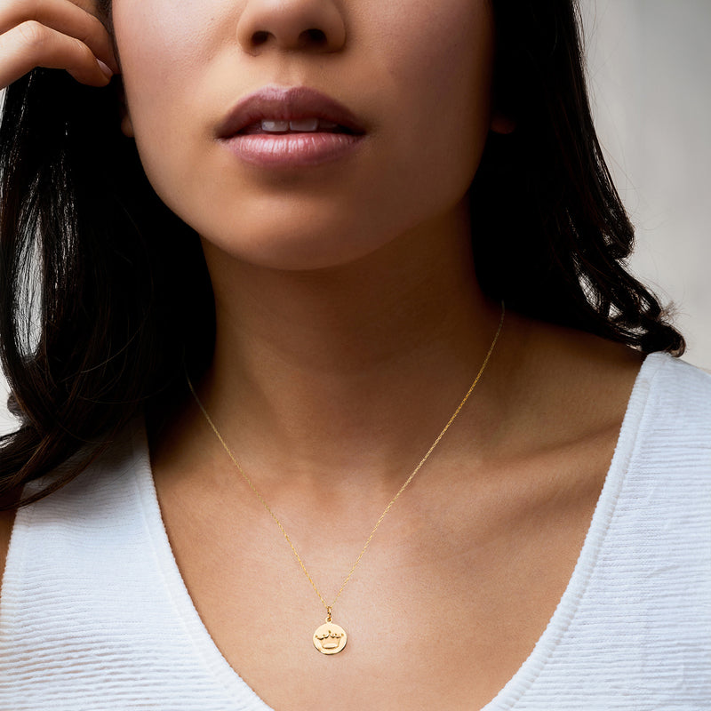 Gold crown disc pendant necklace worn on a thin chain with a small round medallion