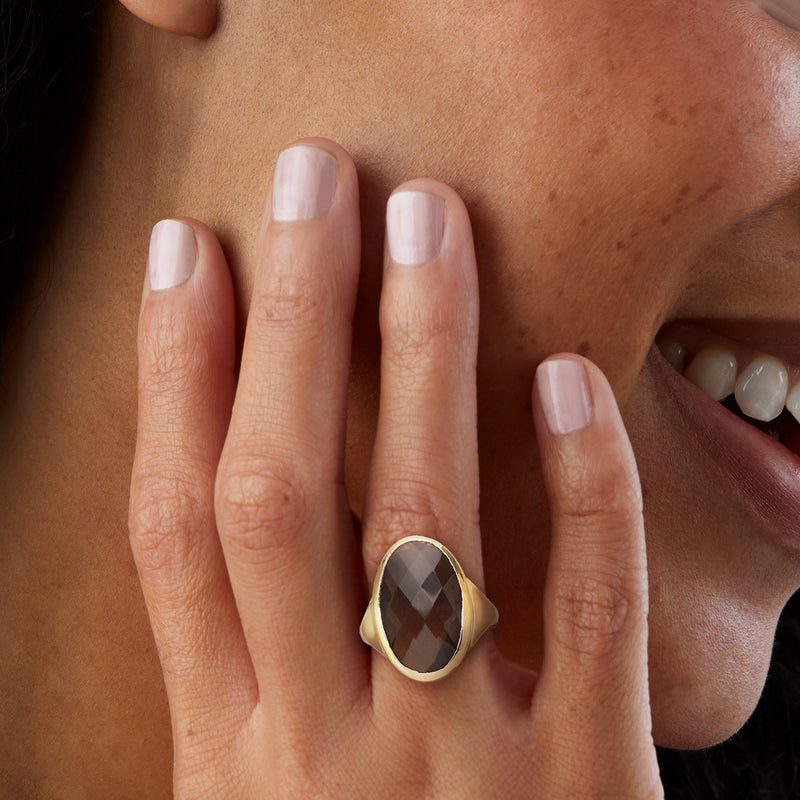 Yellow gold-plated ring with oval smoky quartz on finger, dark faceted stone