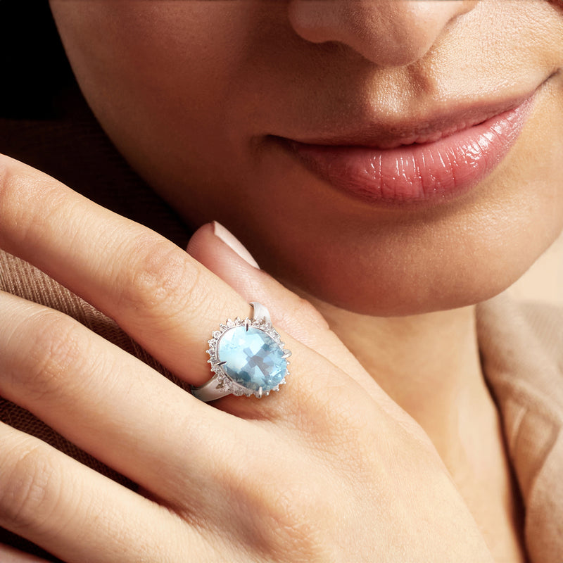 Platinum aquamarine halo ring with oval light-blue gemstone and diamond accents on finger
