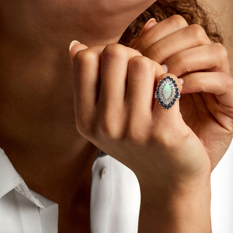Opal halo ring on hand: teardrop opal center with blue sapphires and diamond border