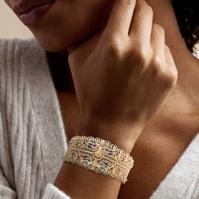 Gold-plated floral filigree cuff bracelet worn on wrist, openwork floral lattice