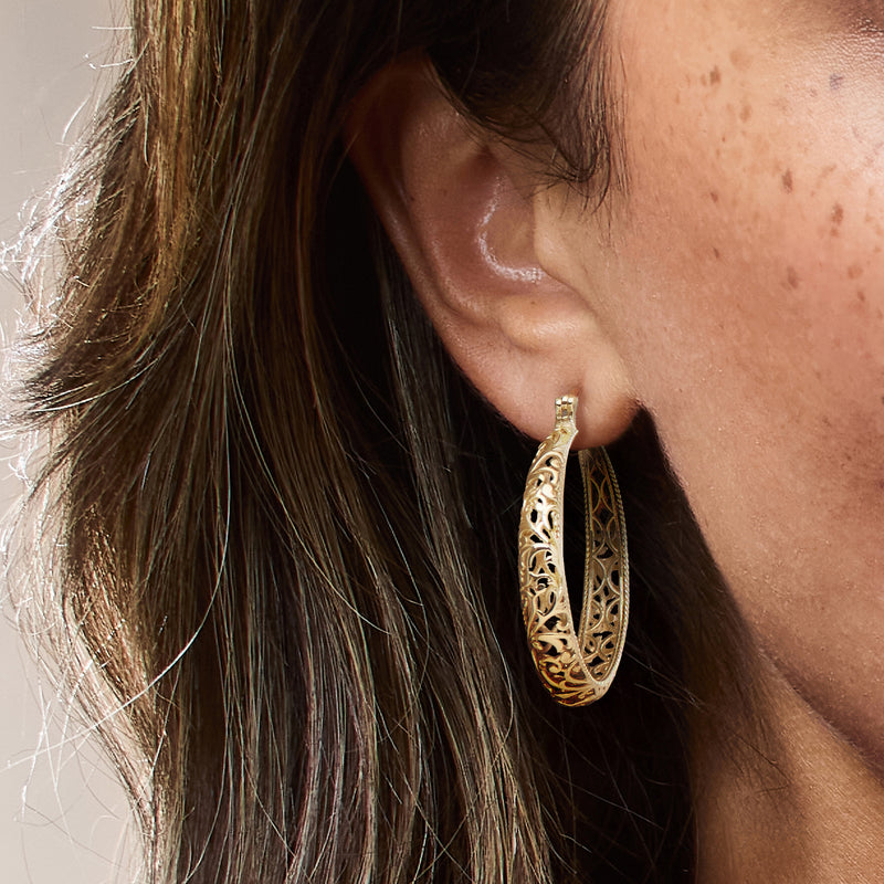 Gold-plated scrollwork hoop earrings worn on ear, textured braided edge
