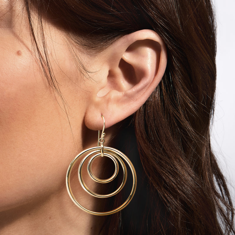 Gold-plated triple-circle drop earrings on ear, layered round loops