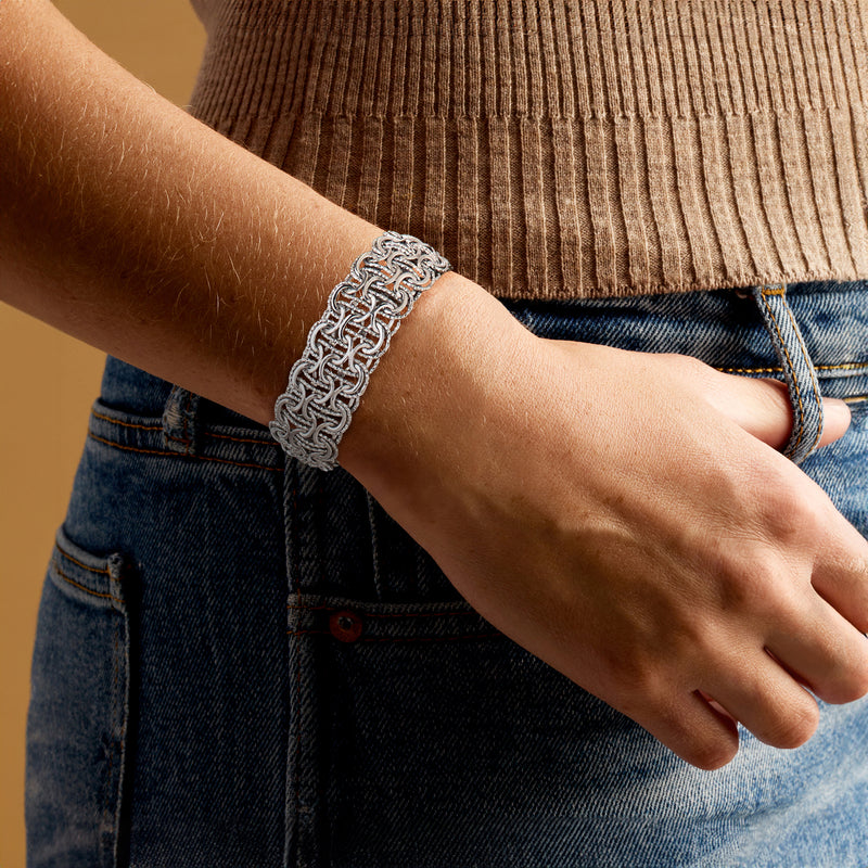 Rhodium-plated woven-link bracelet worn on wrist, shiny silver chain links