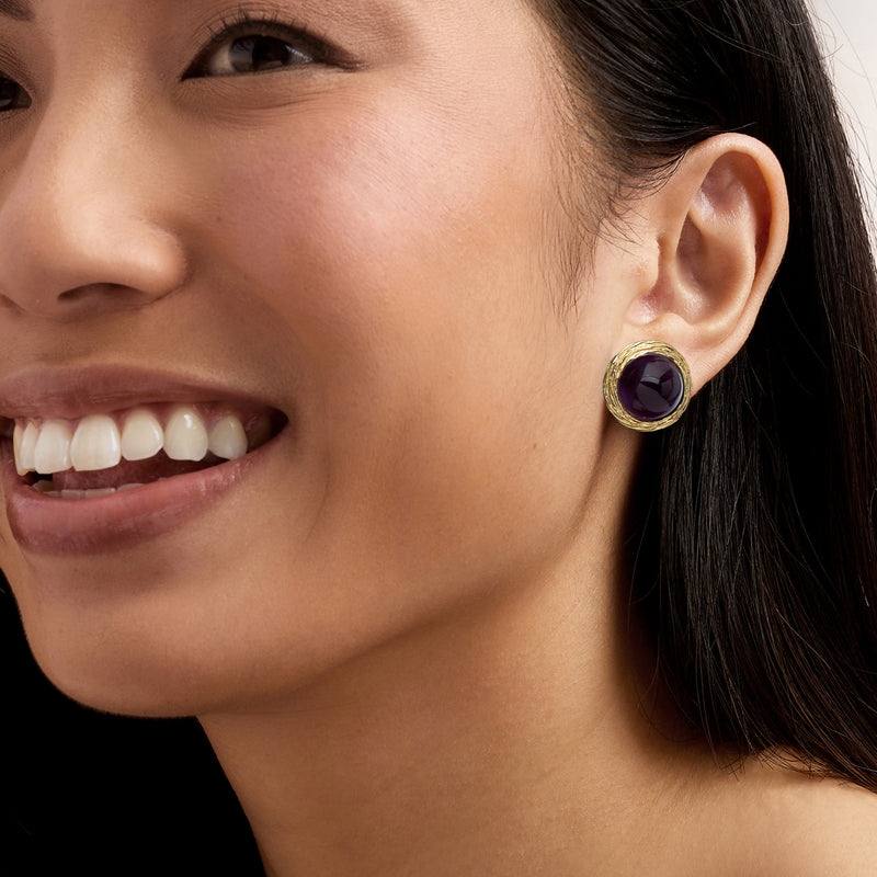 Amethyst ear stud with round purple gemstone in gold frame, close-up on model
