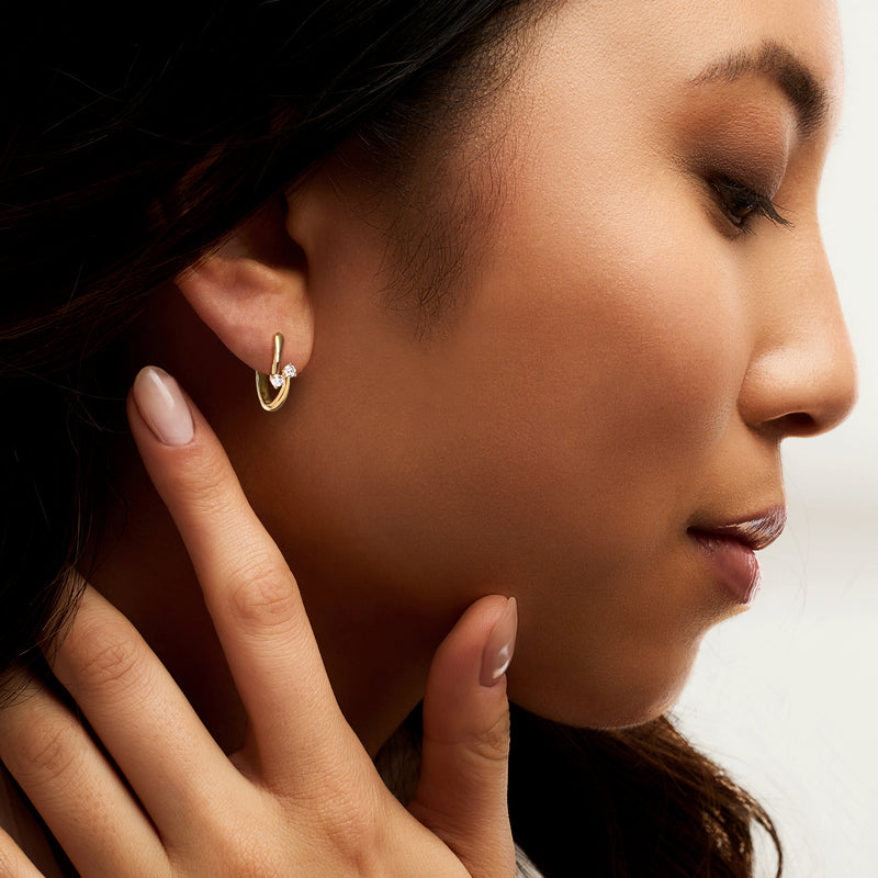 Gold hoop earring on ear with overlapping design and small diamond cluster
