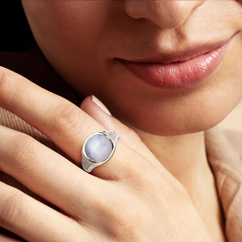 Star sapphire ring on finger: gray oval cabochon with white-gold band and diamond details