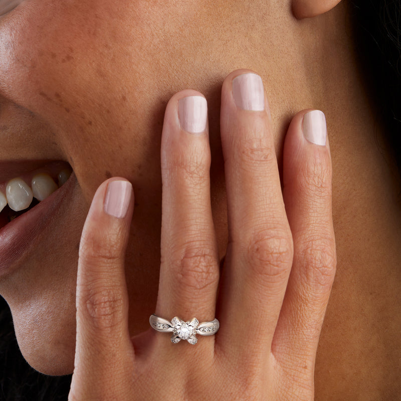 White gold prong-set diamond ring worn on hand with center stone and side accents
