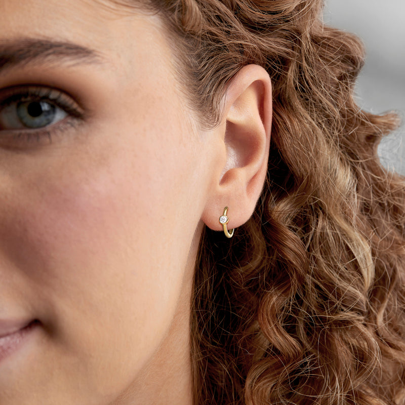 Gold hoop earrings with small bezel-set round diamond on model
