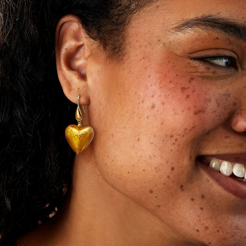 Amber heart drop earrings with gold-tone earwire, worn with small glass charm