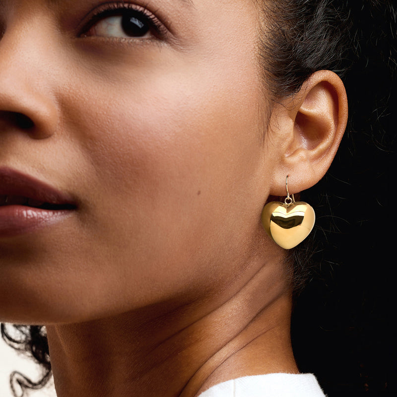 Yellow gold heart drop earrings on ear with hook-style earwire