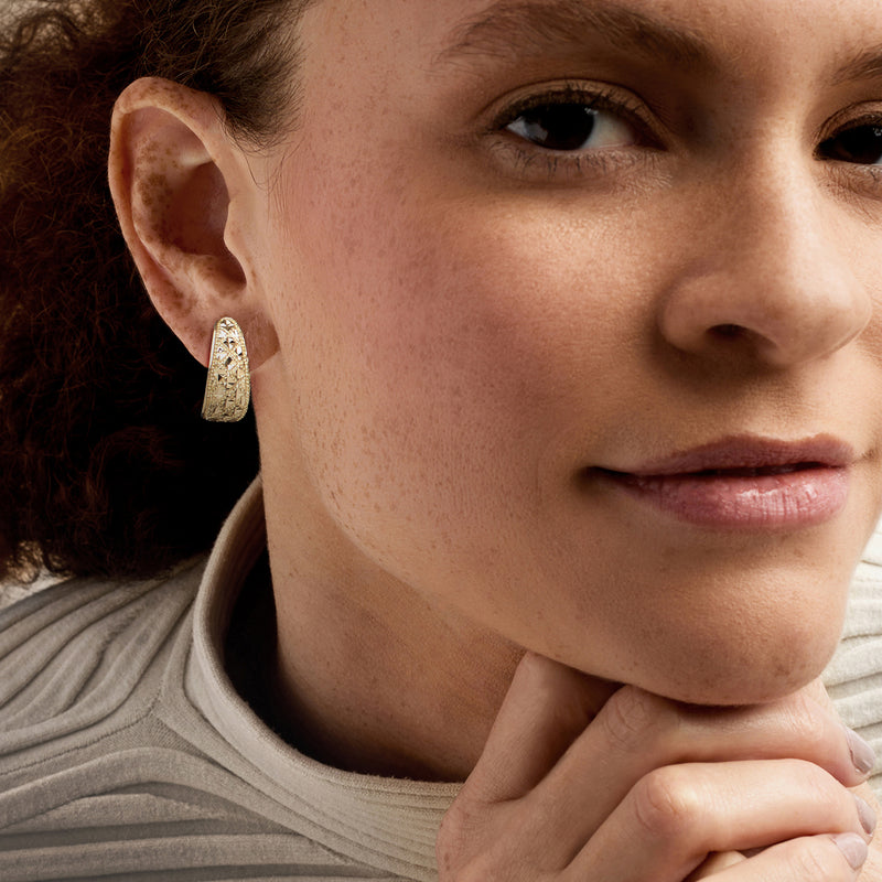 Yellow gold textured curved hoop post earrings on ear, close-up.