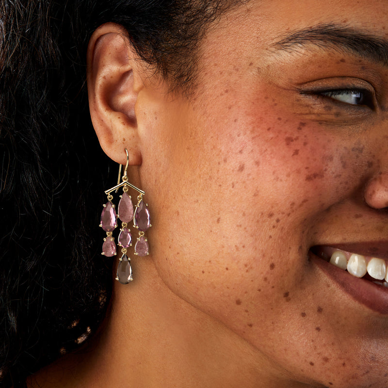 Chandelier drop earrings worn on ear, gold-tone with purple and pink teardrop stones