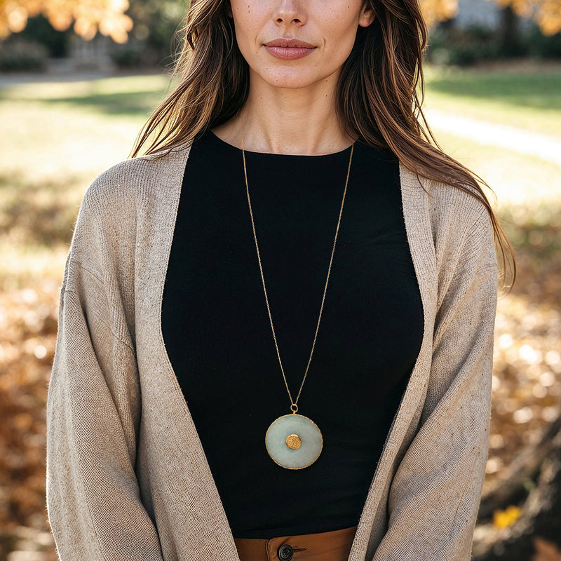 Jade pendant necklace in 14kt yellow gold on model; round pale jade disc with gold seal