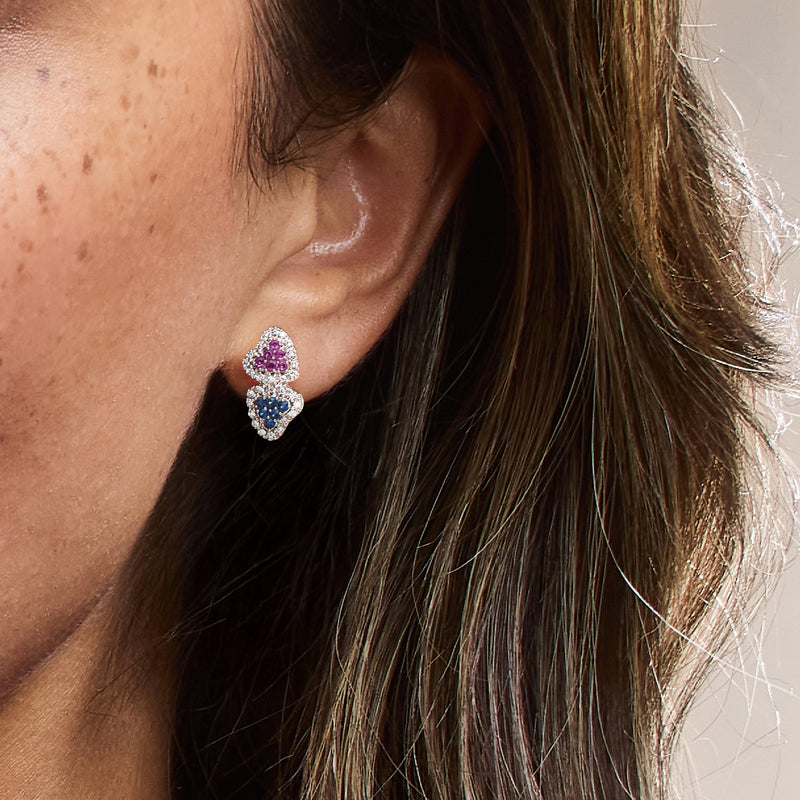 Model wearing heart stud earrings with pink and blue sapphires and diamond accents