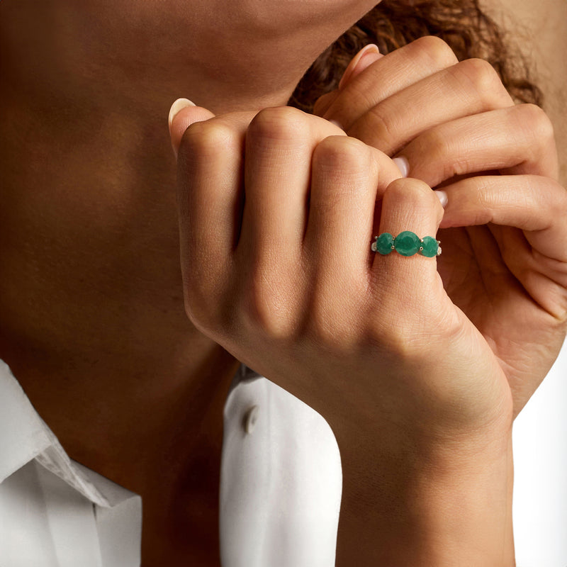 Three-stone green gemstone ring on finger, gold-tone band with prong settings