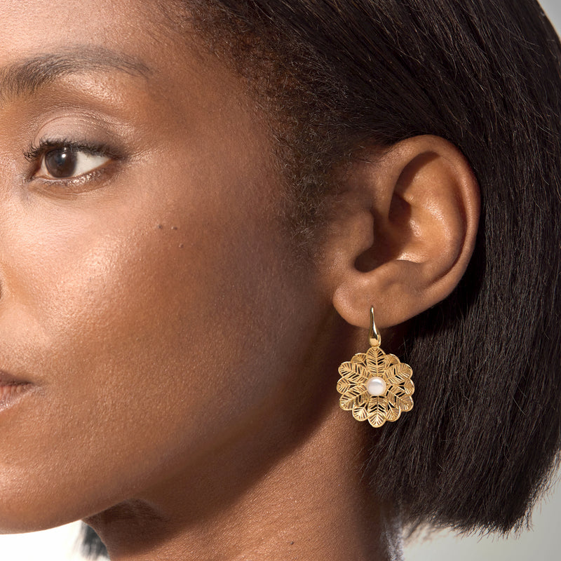 Gold flower drop earrings with round pearl centers on ear hook, close-up