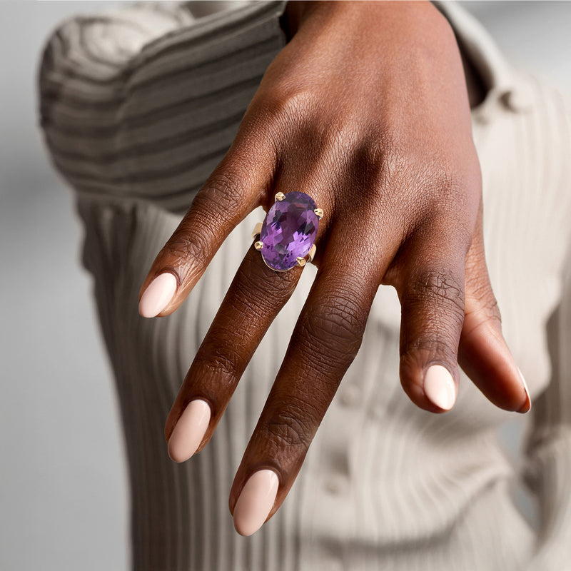 Amethyst ring on finger with oval purple stone and yellow gold band