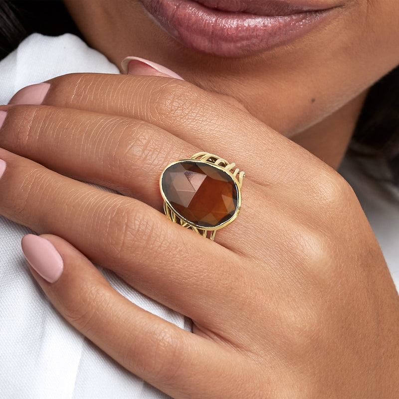 Yellow gold-plated oval brown gemstone ring worn on hand, faceted simulated quartz