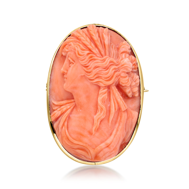 Oval coral cameo pendant in 14kt yellow gold with left-facing profile; pin clasp visible.