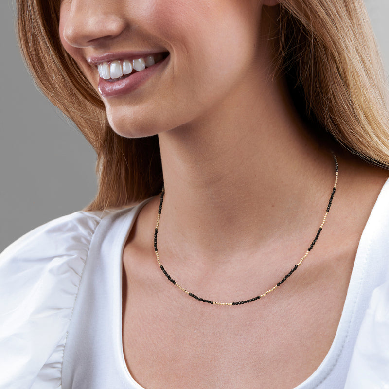 Black bead necklace with yellow gold micro spacer beads, worn at the collar