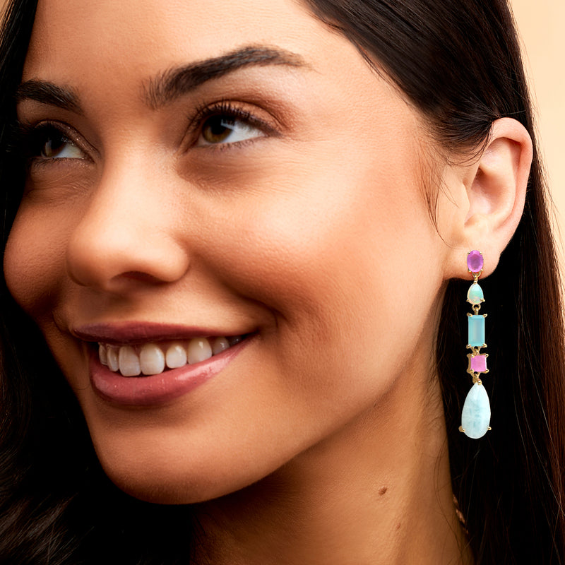 Gold-tone drop earrings on ear with purple top and light blue teardrop gemstones