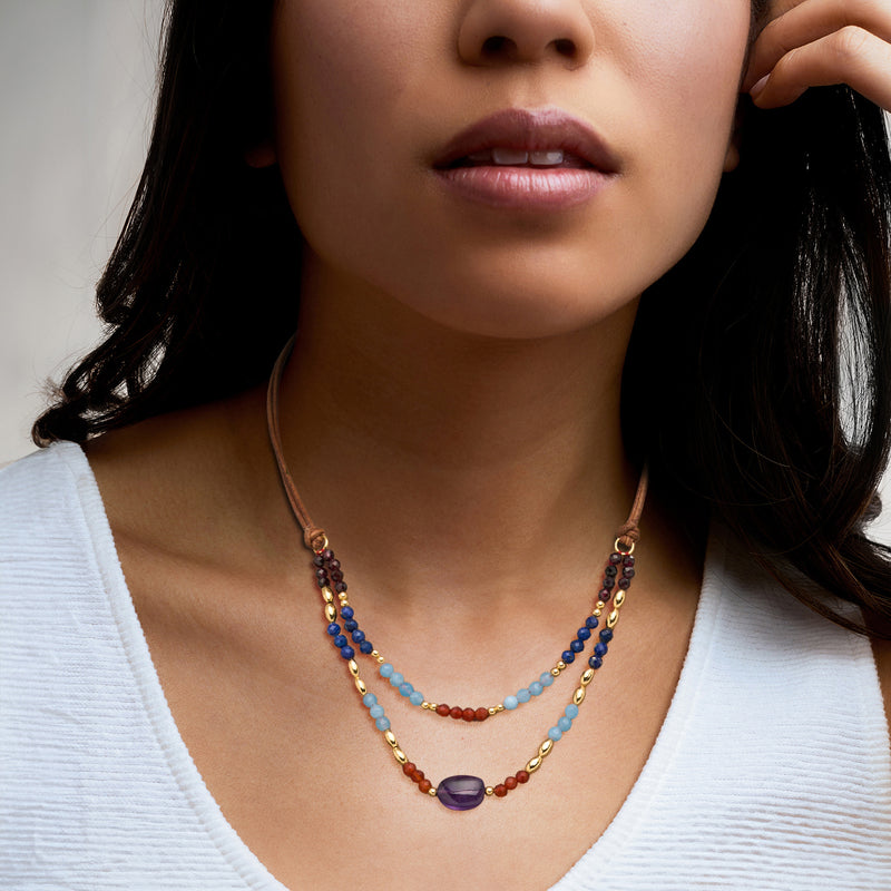 Layered bead necklace on model with brown leather cord, multicolor beads and purple charm