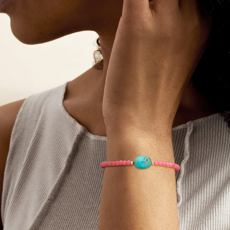 Pink coral beaded bracelet with turquoise oval charm on wrist, gold clasp detail.