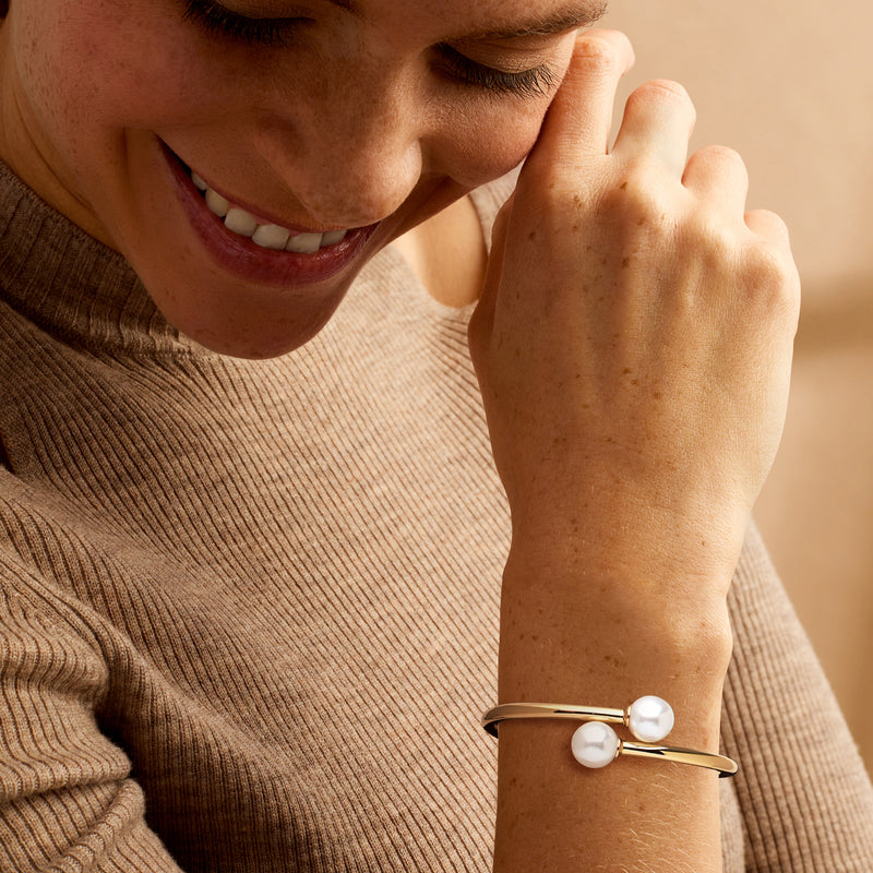 Yellow gold-plated bypass bracelet with two white simulated pearls on wrist