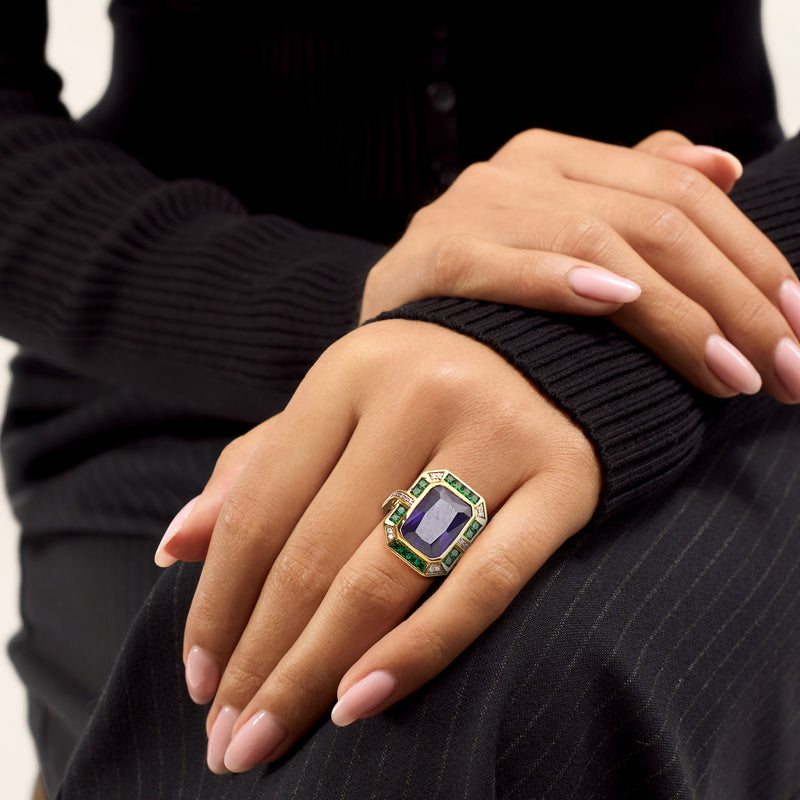 Ring on hand: yellow gold-plated band with purple center stone, green side stones, CZ
