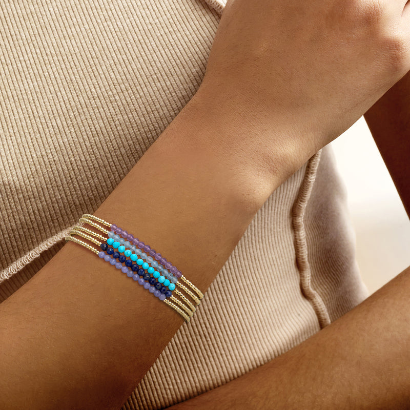 Wrist wearing gold-tone bead stretch bracelets with purple, blue and teal bead rows