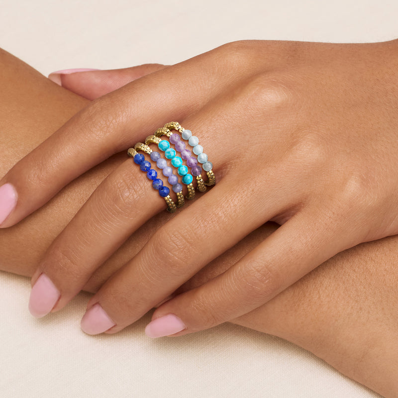 Five gold-plated bead stretch rings on hand, light blue, purple, dark blue, and turquoise