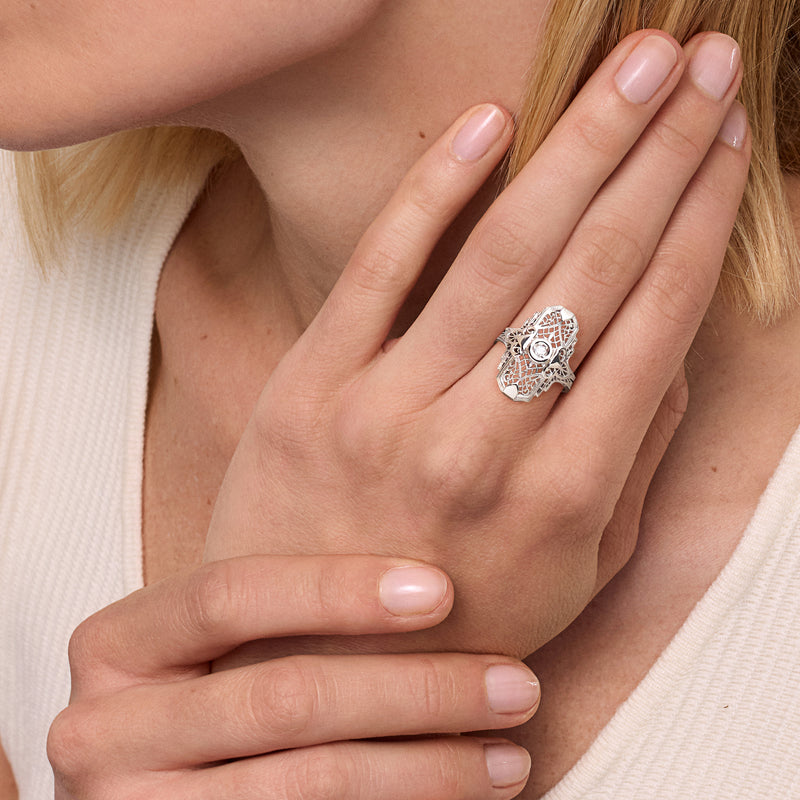 Diamond filigree ring with round center stone on finger, ornate white-gold setting