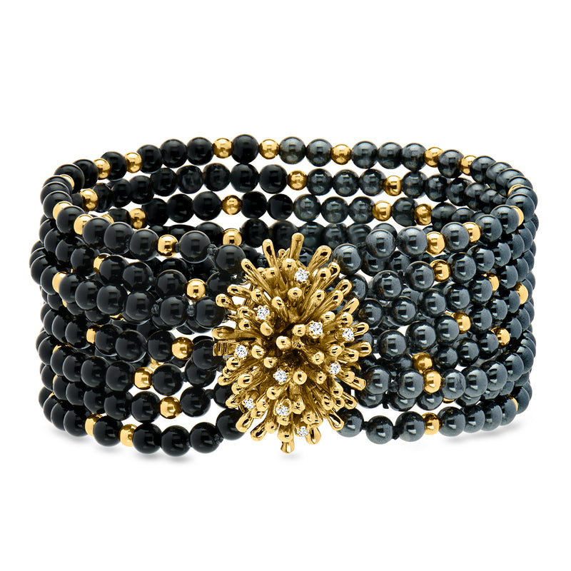 Multi-row beaded bracelet with dark round beads and a gold flowerburst centerpiece