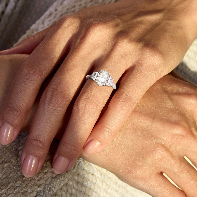 White gold lab-grown diamond ring on hand, oval center stone with small side diamonds