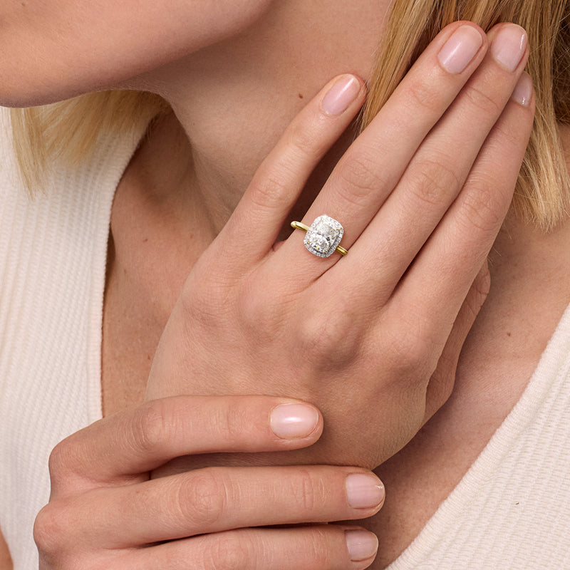 Cushion-cut diamond halo ring on hand with yellow gold band