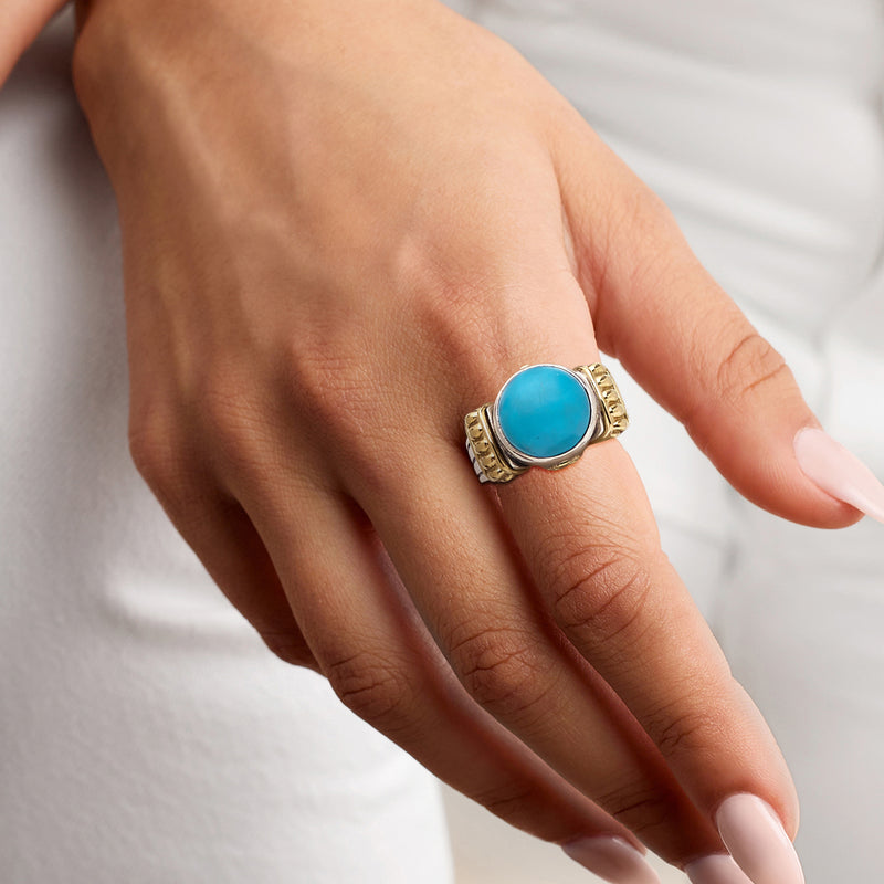 Turquoise cabochon ring on hand; sterling silver band with 18kt yellow gold accents
