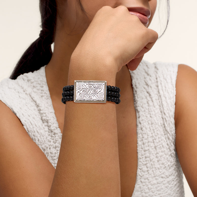 Black bead stretch bracelet on wrist with silver rectangular centerpiece and gold border