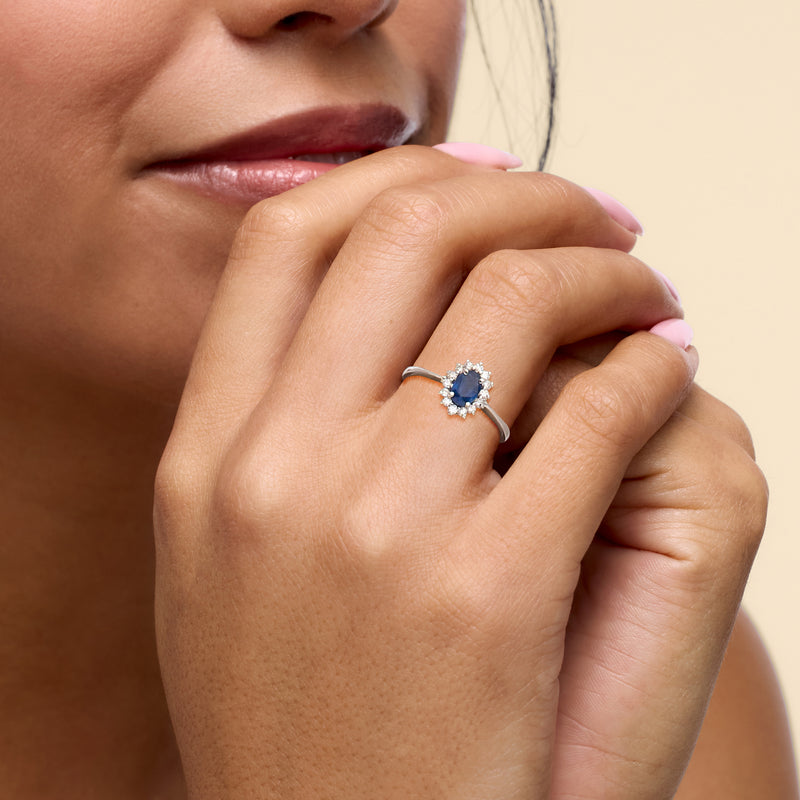 Diamond halo sapphire ring on hand with oval blue stone in 18kt white gold