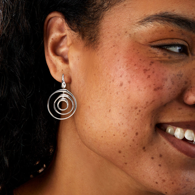 Sterling silver spiral drop earrings worn on ear with concentric oval rings