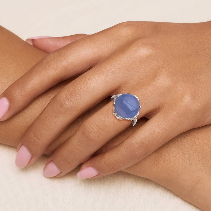 Blue-lavender oval gemstone ring with diamond halo on finger, white gold prongs