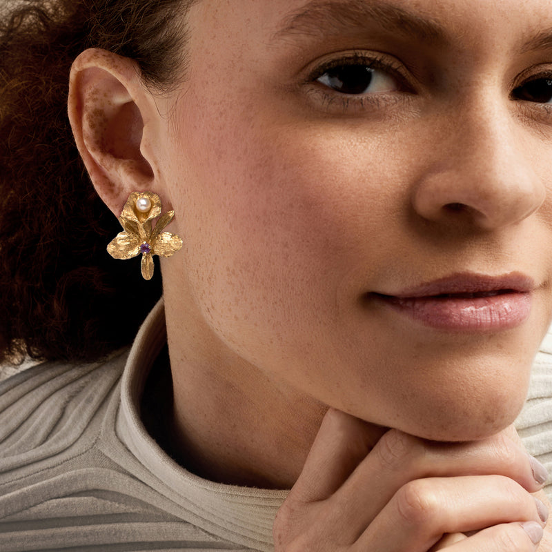 Gold orchid clip earrings with white pearl and purple amethyst, worn side view