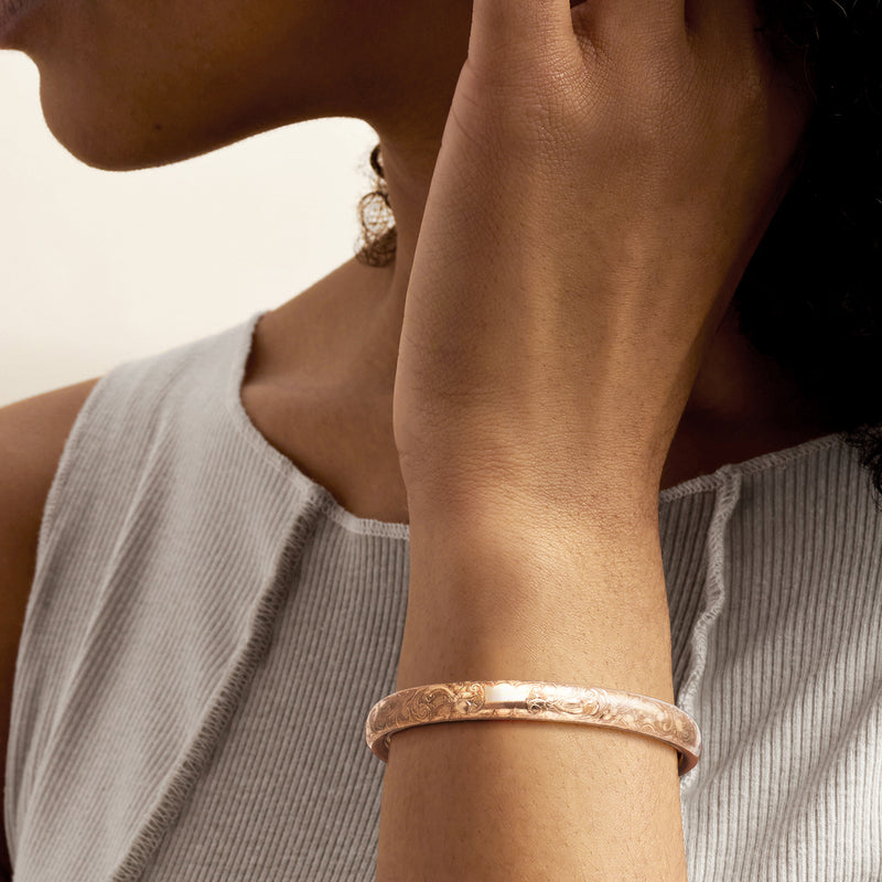 Gold-toned floral etched bangle on wrist with hinged clasp