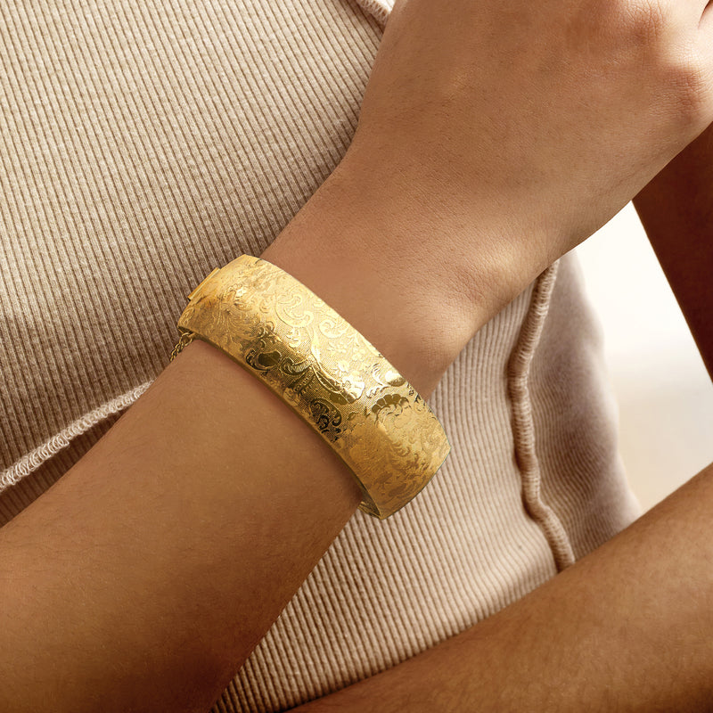 Gold-tone wide bangle bracelet with engraved floral etching worn on wrist