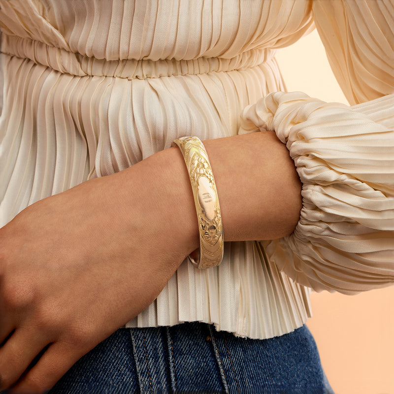 Gold-filled floral etched bangle bracelet worn on wrist, smooth interior and engraved panel