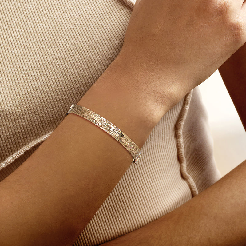 Gold-tone etched feather bangle bracelet on wrist, hinged clasp visible